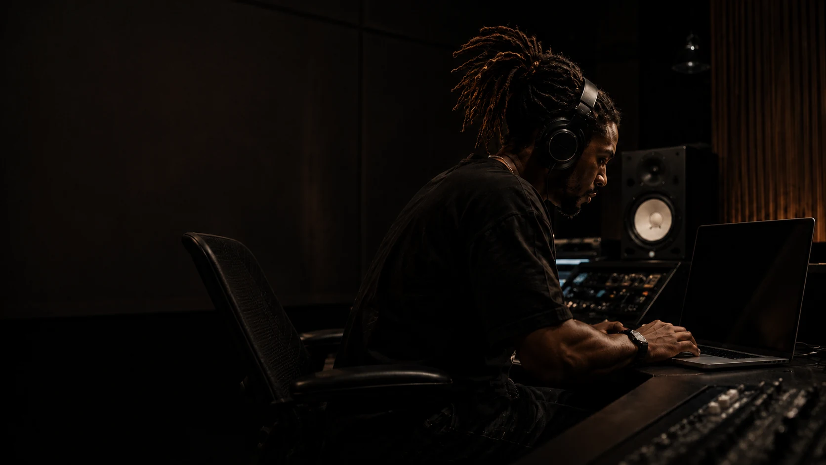 A creator wearing headphones works on a laptop in a recording studio.